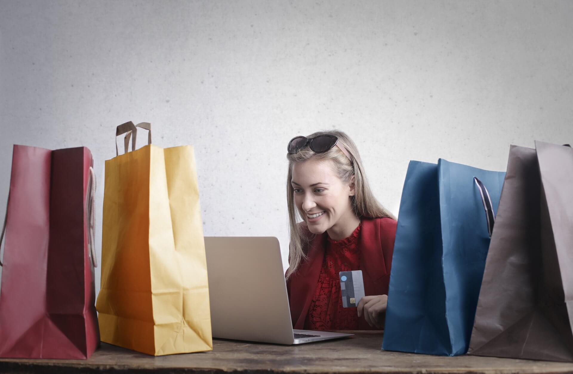 Happy woman sitting doing online shopping holding credit card with many shopping bags on table