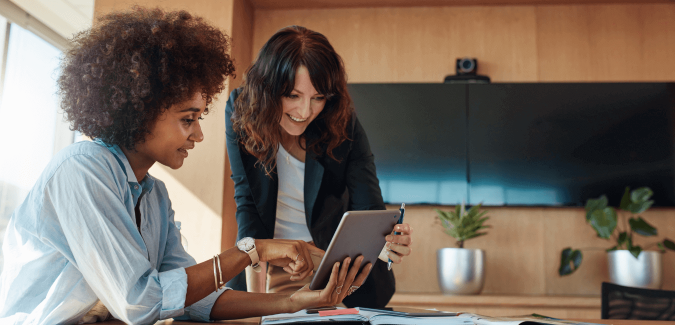 Two women chatting in the office while looking at something on an iPad.