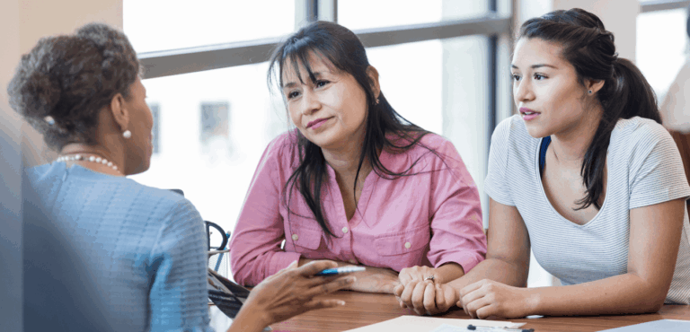Mother and daughter sitting face to face with a loan officer, listening carefully