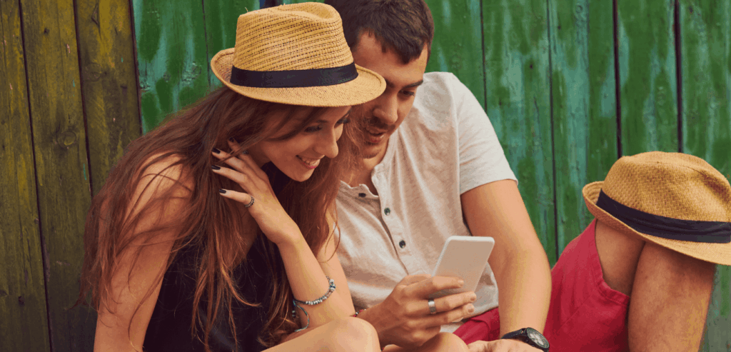Young couple looking at a cellphone outdoors with another person nearby