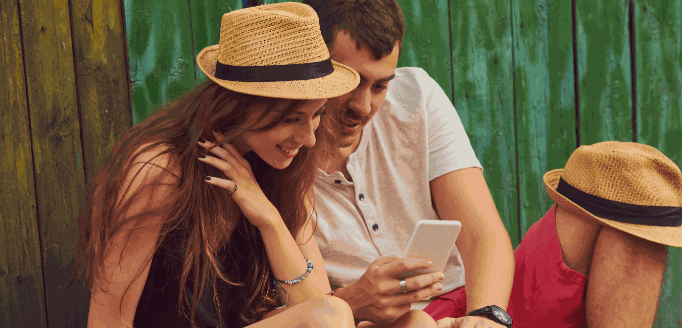 Young couple looking at a cellphone outdoors with another person nearby