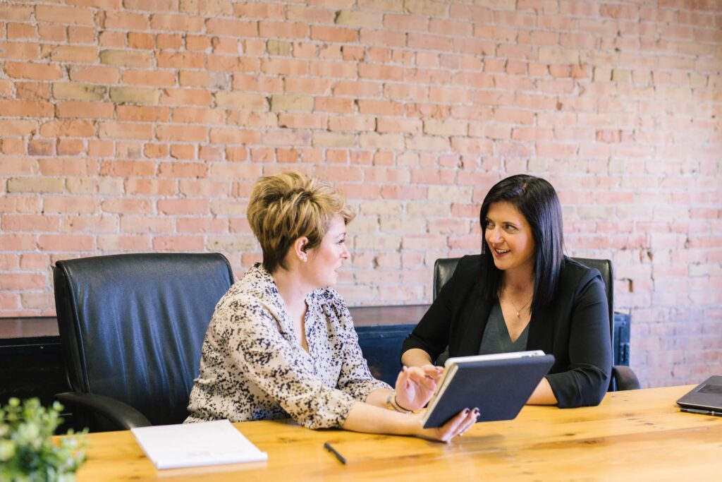 Two women discuss information on a tablet at a table in an office