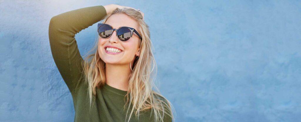 Smiling woman in sunglasses posing against a blue background