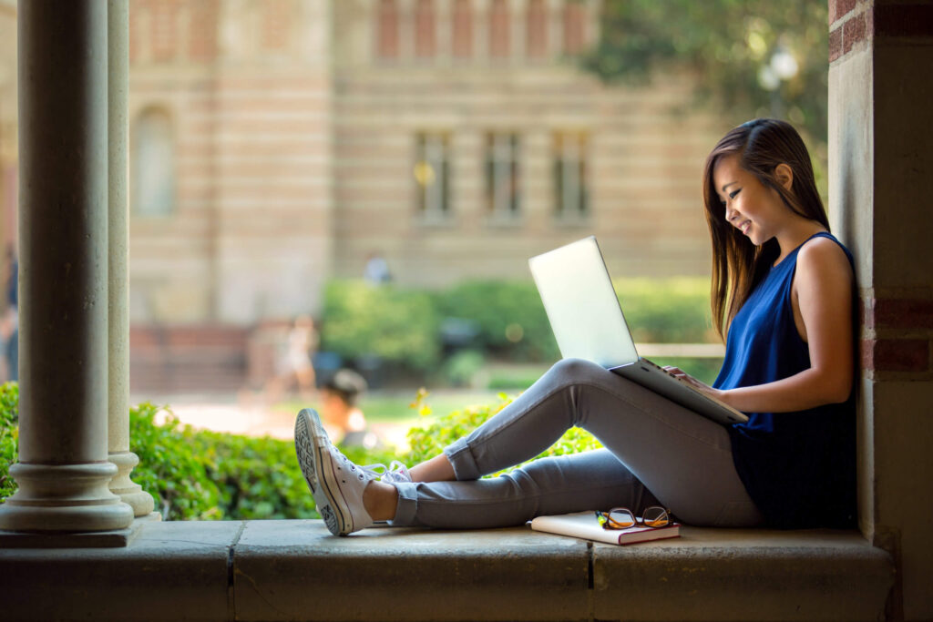 Young woman using a laptop while sitting on a building's porch